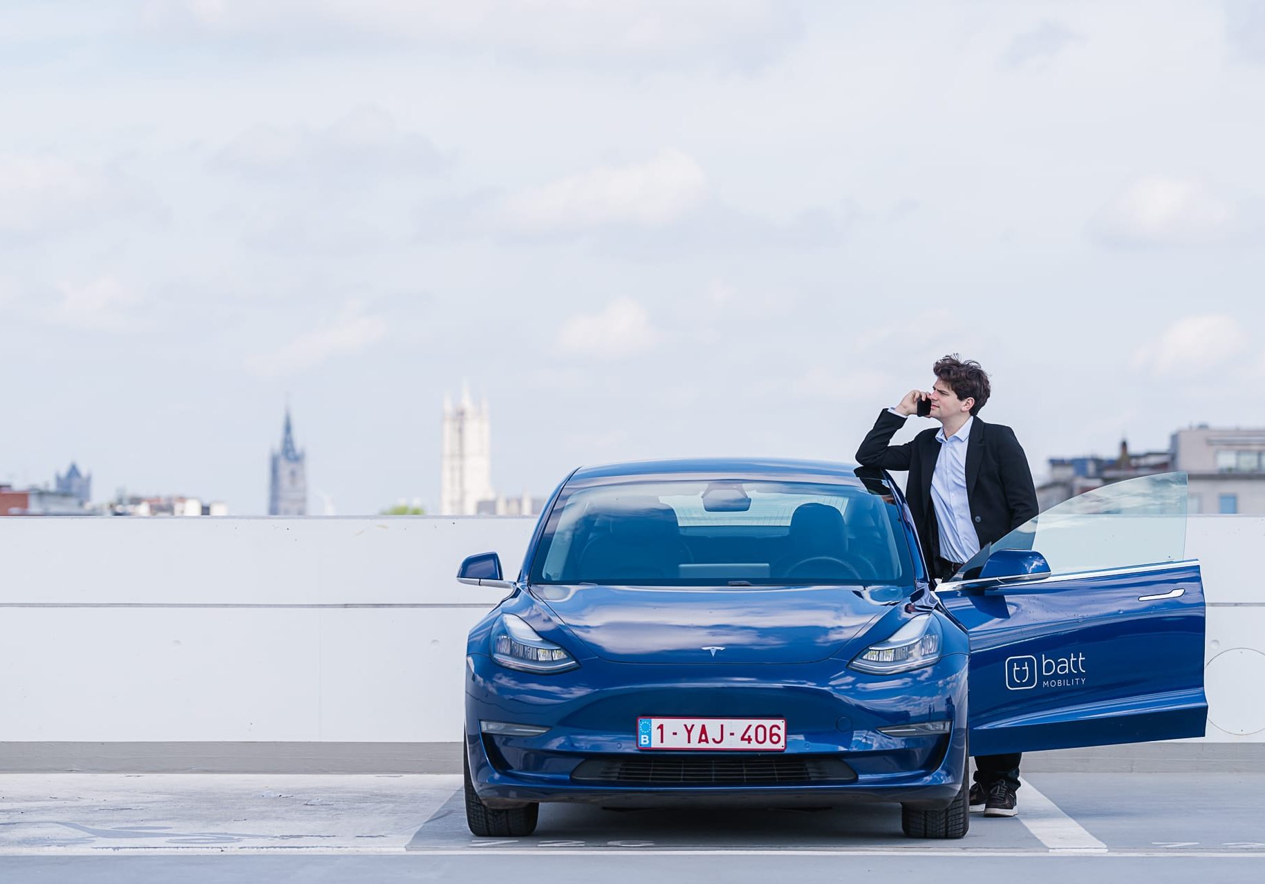 Man bij elektrische deelwagen van BattMobility met in de achtergrond de skyline van Gent.